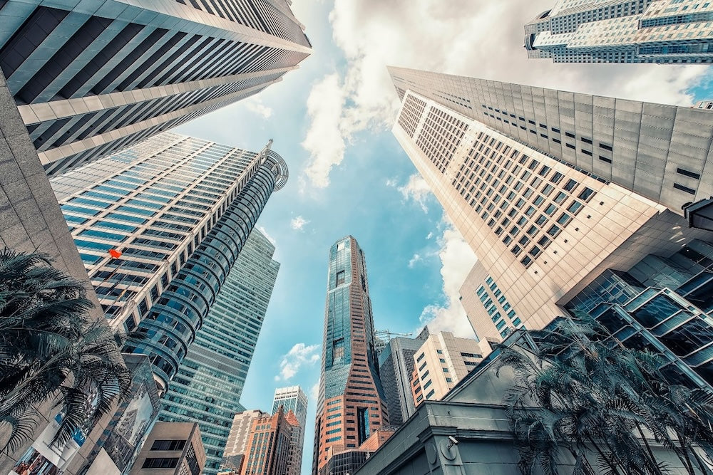 Tall skyscrapers in Singapore’s Central Business District rise toward the sky, captured from a low angle with bright clouds above.