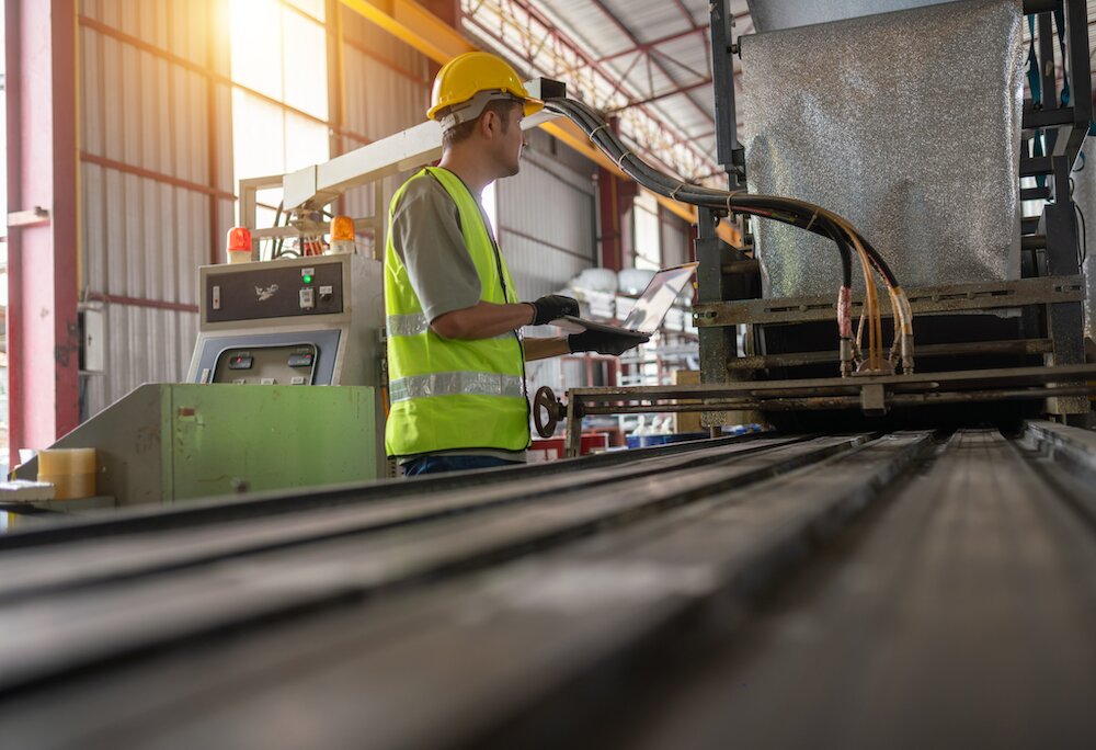 Factory technician operating industrial machinery with a laptop on the production floor in a modern manufacturing facility.