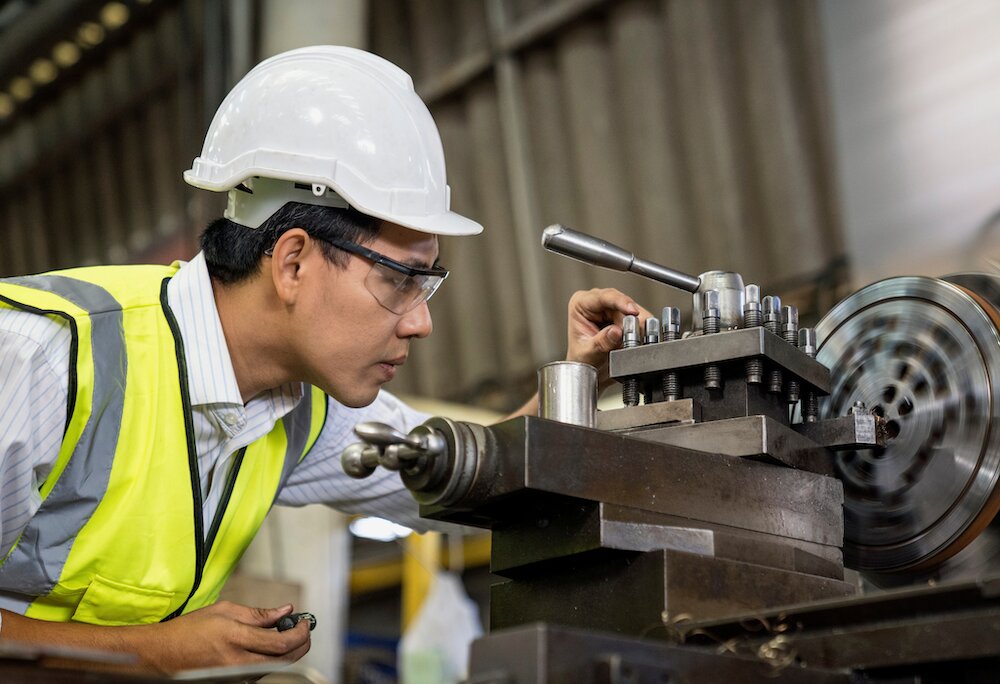 Engineer inspecting a metal lathe machine in a precision engineering workshop within the manufacturing sector.